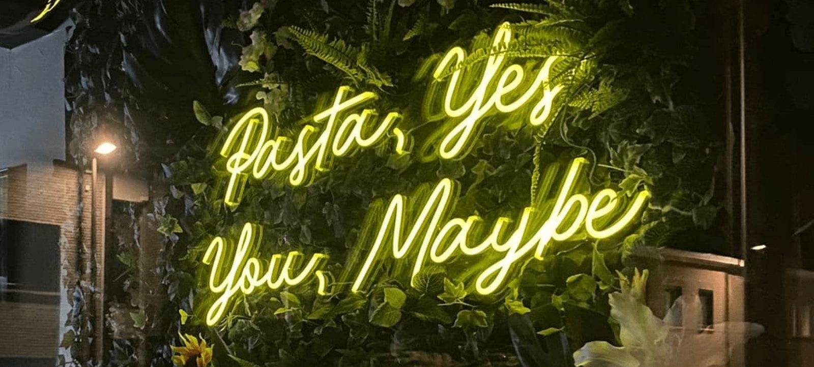 Neonverlichting "Pasta, Yes. You, Maybe" tussen het groen in het restaurant